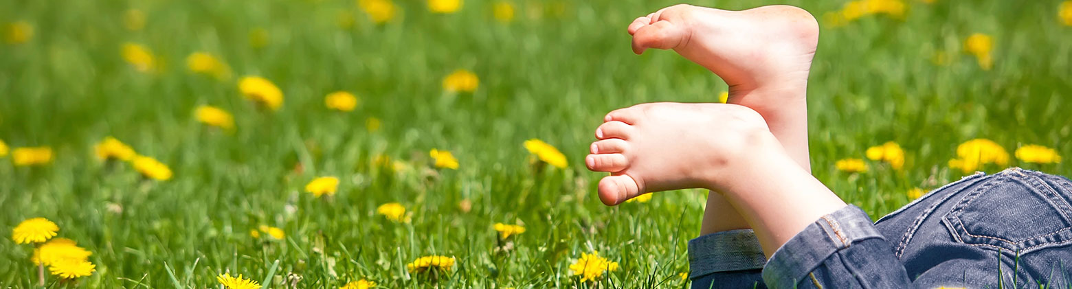 WMS – Passt natürlich! Kind liegt barfuß auf Blumenwiese